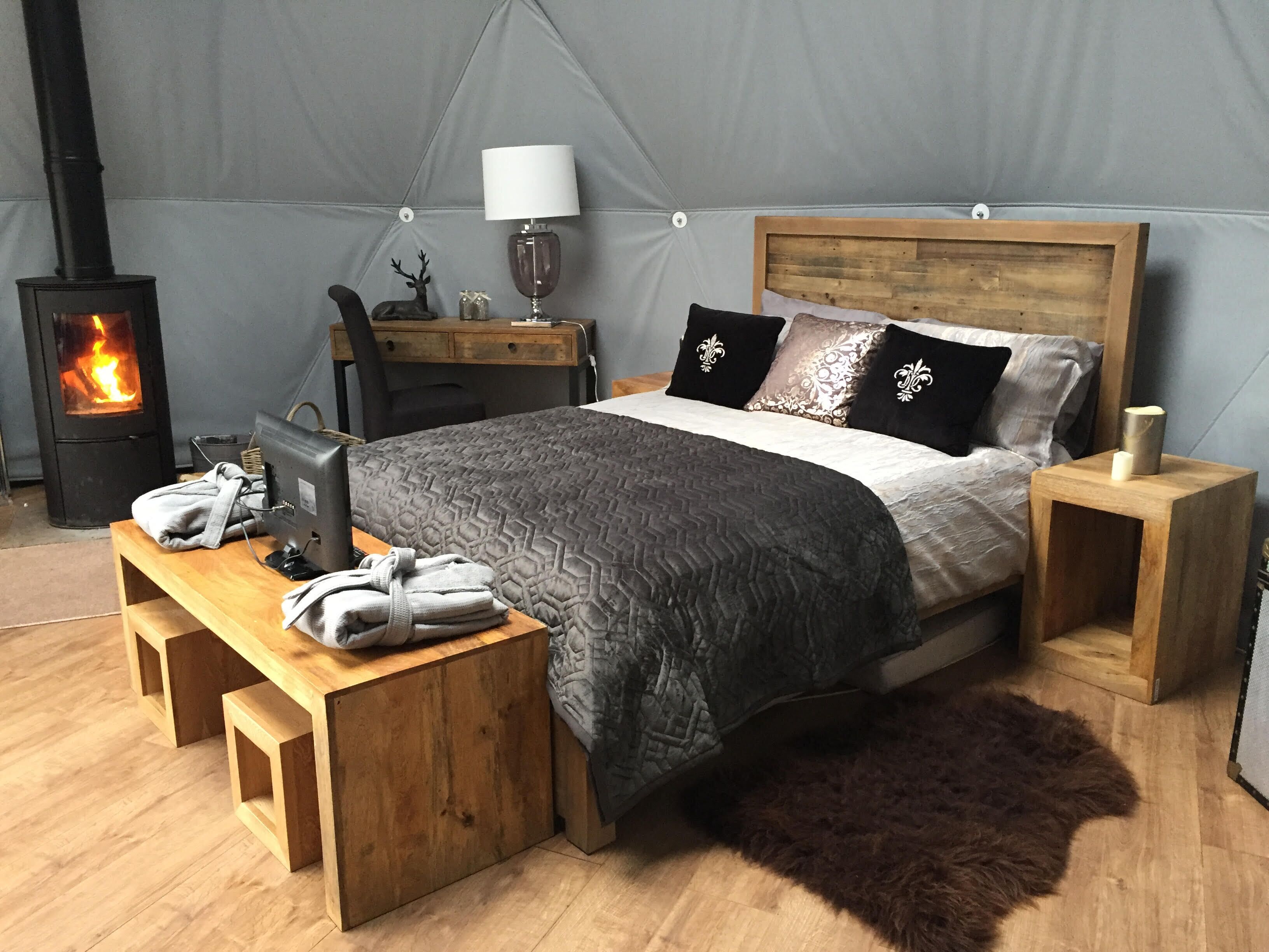 Een gezellige slaapkamer met een bed, houten nachtkastjes, een bureau, een lamp en een houtkachel.