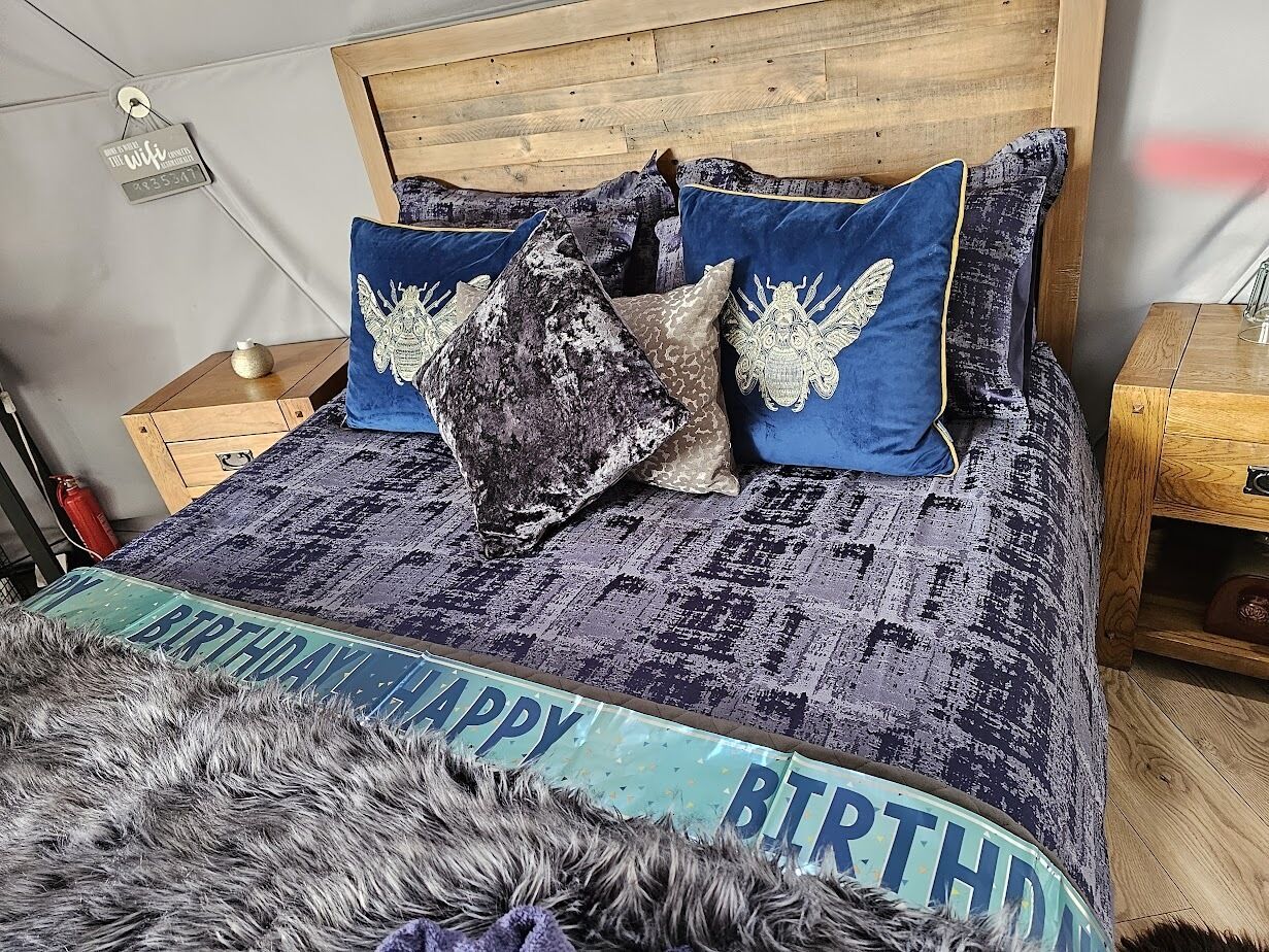 Un dormitorio con cabecera de madera, ropa de cama estampada y un cartel que dice 'Feliz Cumpleaños' sobre la cama.