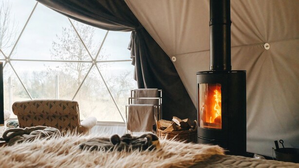 Ein gemütliches Zimmer mit großem Fenster, Kamin, Sessel und Fellteppich.