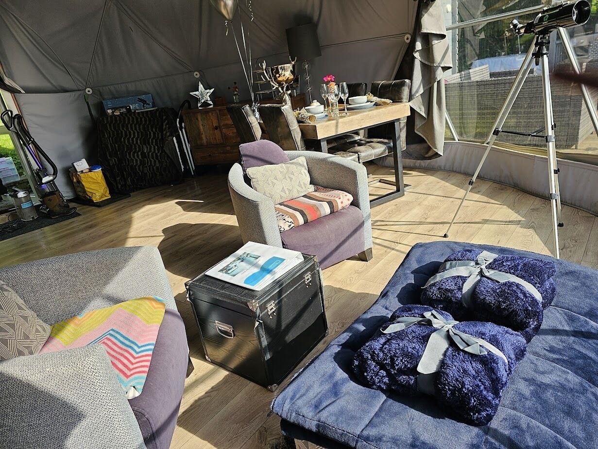 Un espacio al aire libre cubierto con una carpa, una mesa de comedor, sillas y un telescopio.