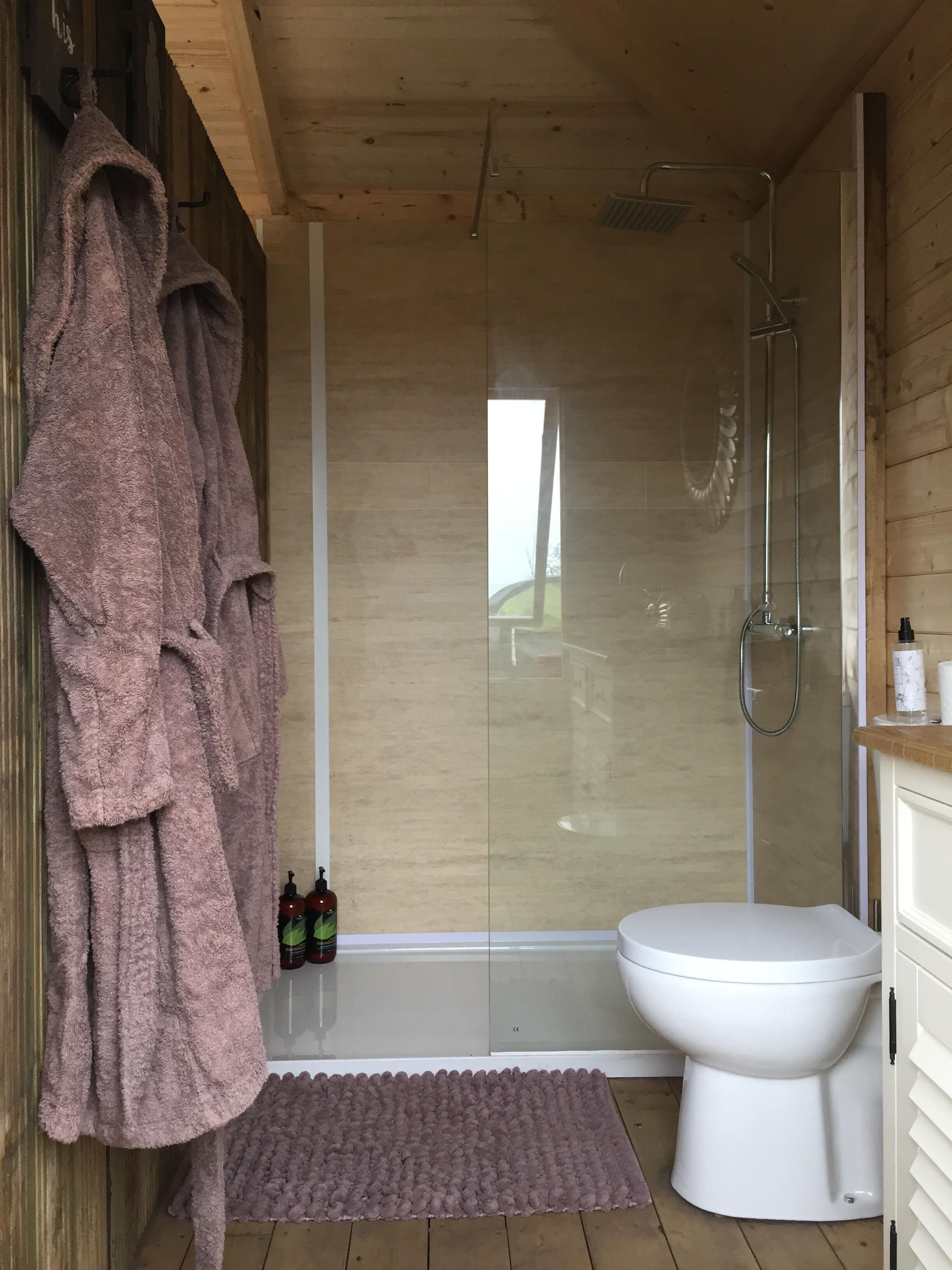 A bathroom with a glass shower enclosure, a white toilet, and a pink bath mat.