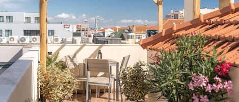 A rooftop terrace with a wooden pergola, a table and chairs, potted plants, and a view of the cityscape.