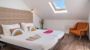A bedroom with two beds, a skylight, a chair, and a vase with flowers.