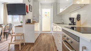 A modern kitchen with a flat-screen TV, wooden flooring, and a view of the city through the window.