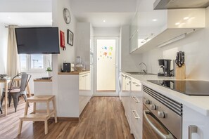 A modern kitchen with a flat-screen TV, wooden flooring, and a view of the city through the window.
