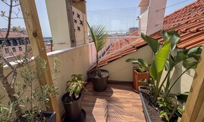 A balcony with potted plants, a wooden railing, and a view of the cityscape.