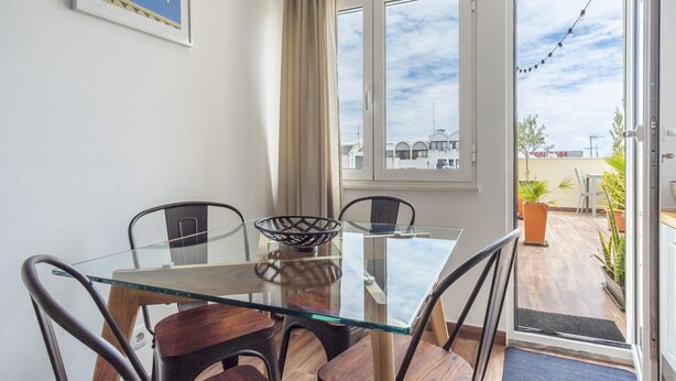 A dining area with a glass table, four chairs, a bowl, and a view through the door to an outdoor patio.