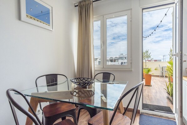 A dining area with a glass table, four chairs, a bowl, and a view through the door to an outdoor patio.