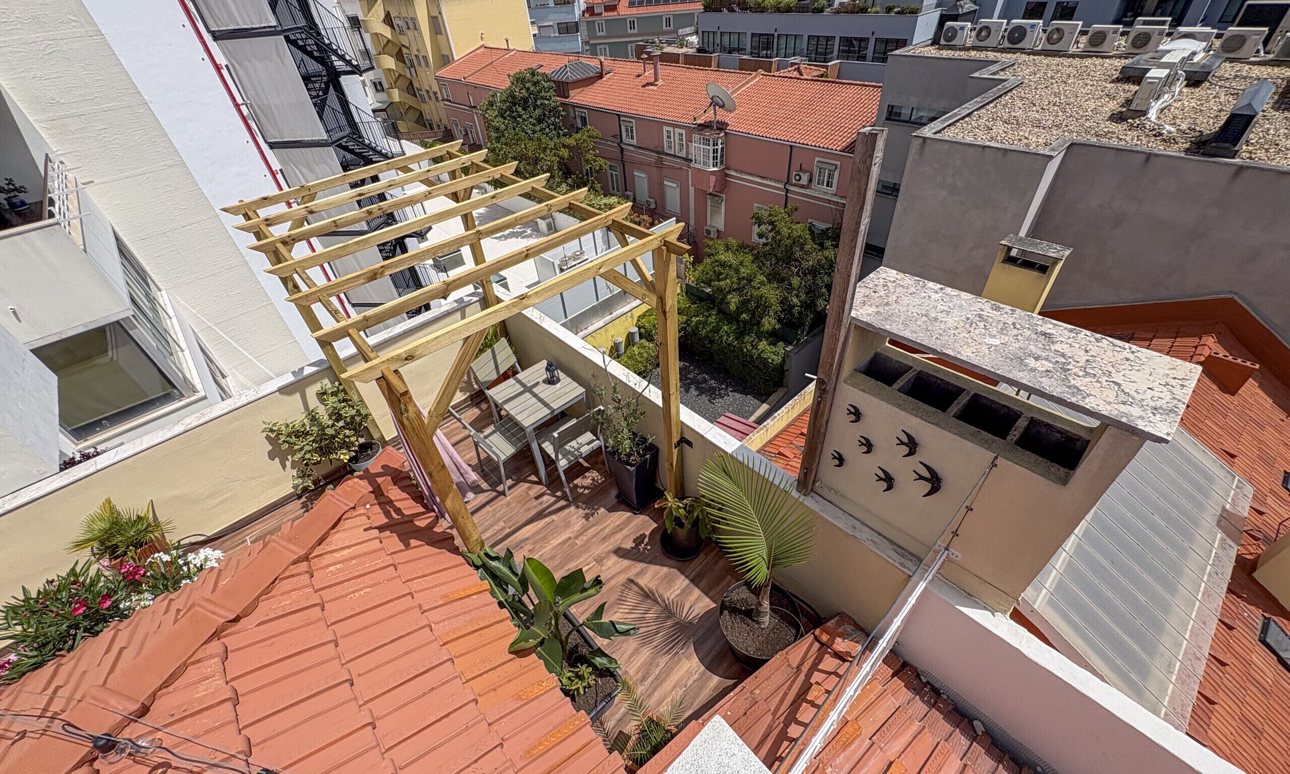 En tagterrasse med en træpergola, plantekasser og udsigt til omkringliggende bygninger.