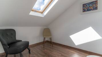 Une pièce avec un plafond en pente, un puits de lumière, une chaise noire, une chaise beige et un plancher en bois.