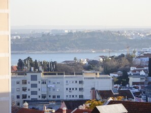 A coastal cityscape with buildings, a body of water, and a hilly background.