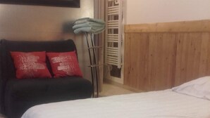Een kamer met een bed, een bank met rode kussens, een elektrische kachel en een houten hoofdeinde.