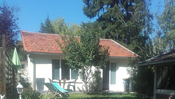 Een huis met een rood pannendak, een kleine tuin met een stenen muur en een terras met een tafel en stoelen.