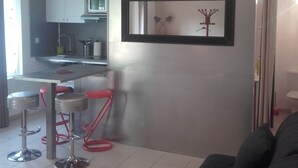 Een moderne woonkamer met een donkere bank, een keuken met witte kastjes en een lijst met een foto aan de muur.