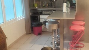 Een kleine keuken met een magnetron, spoelbak en een eethoekje met een tafel en krukjes.