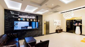 A modern reception area with a black marble wall, a reception desk, a seating area with leather chairs, and a large white vase with flowers.