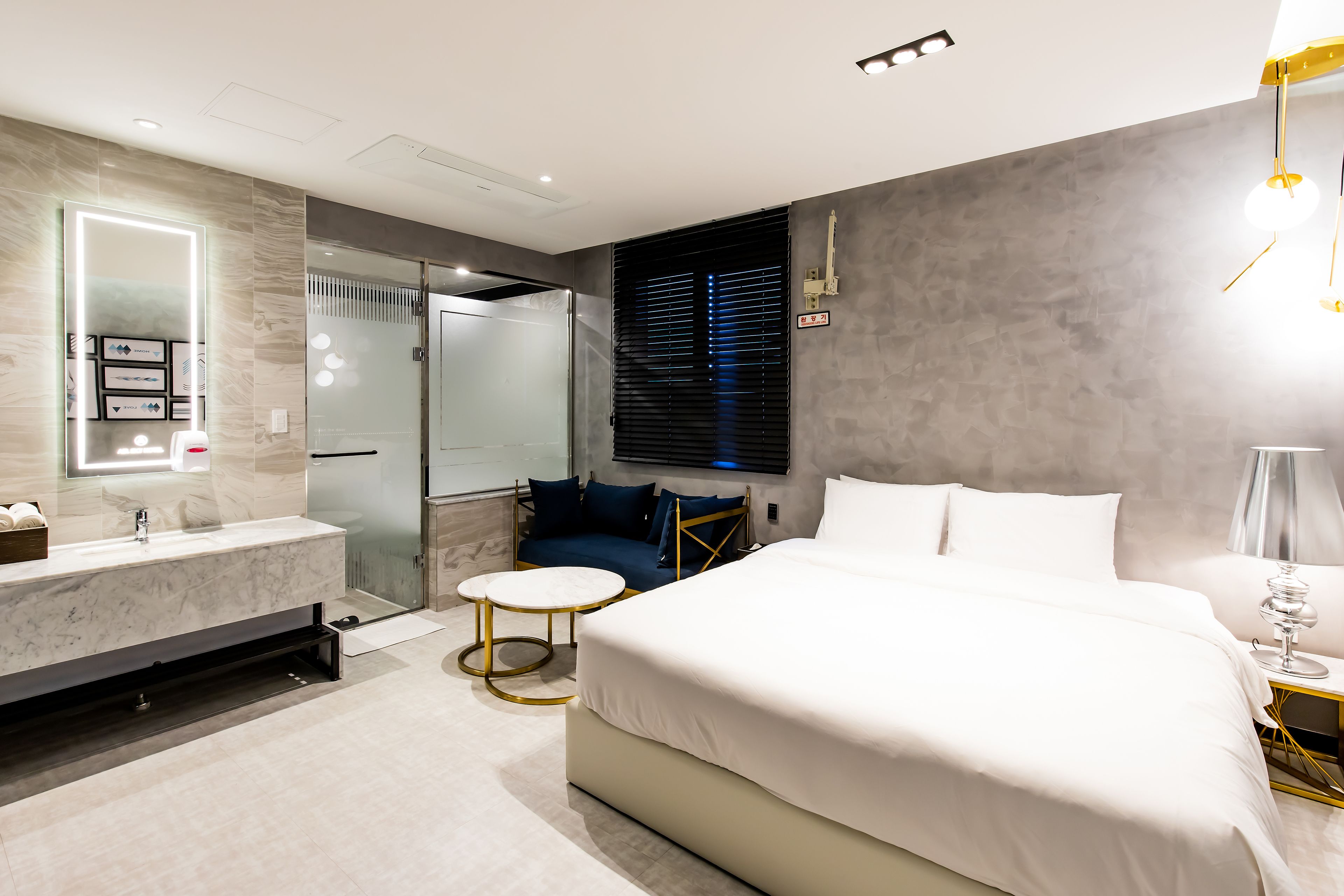 Un dormitorio moderno con una cama grande, un tocador con espejo, un vestidor y una zona de estar con vistas a la ciudad.