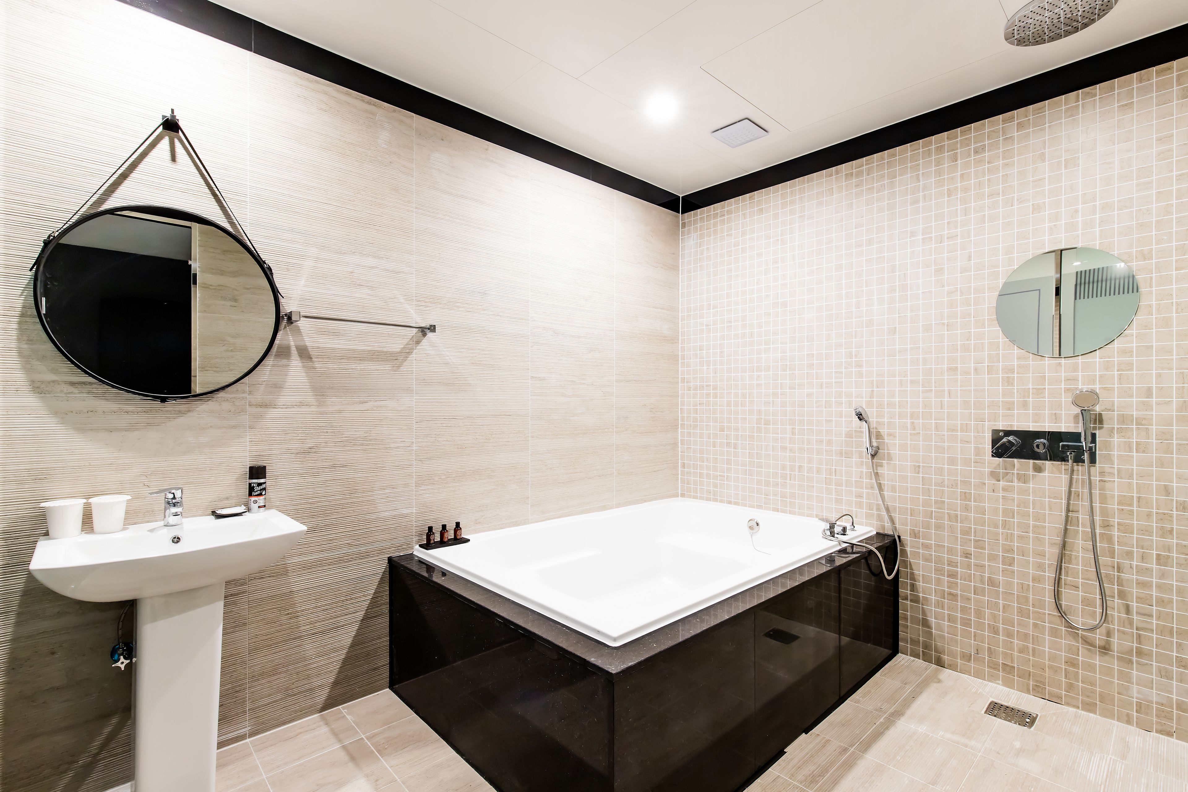 Un baño moderno con un lavabo blanco, una bañera independiente y un espejo redondo.