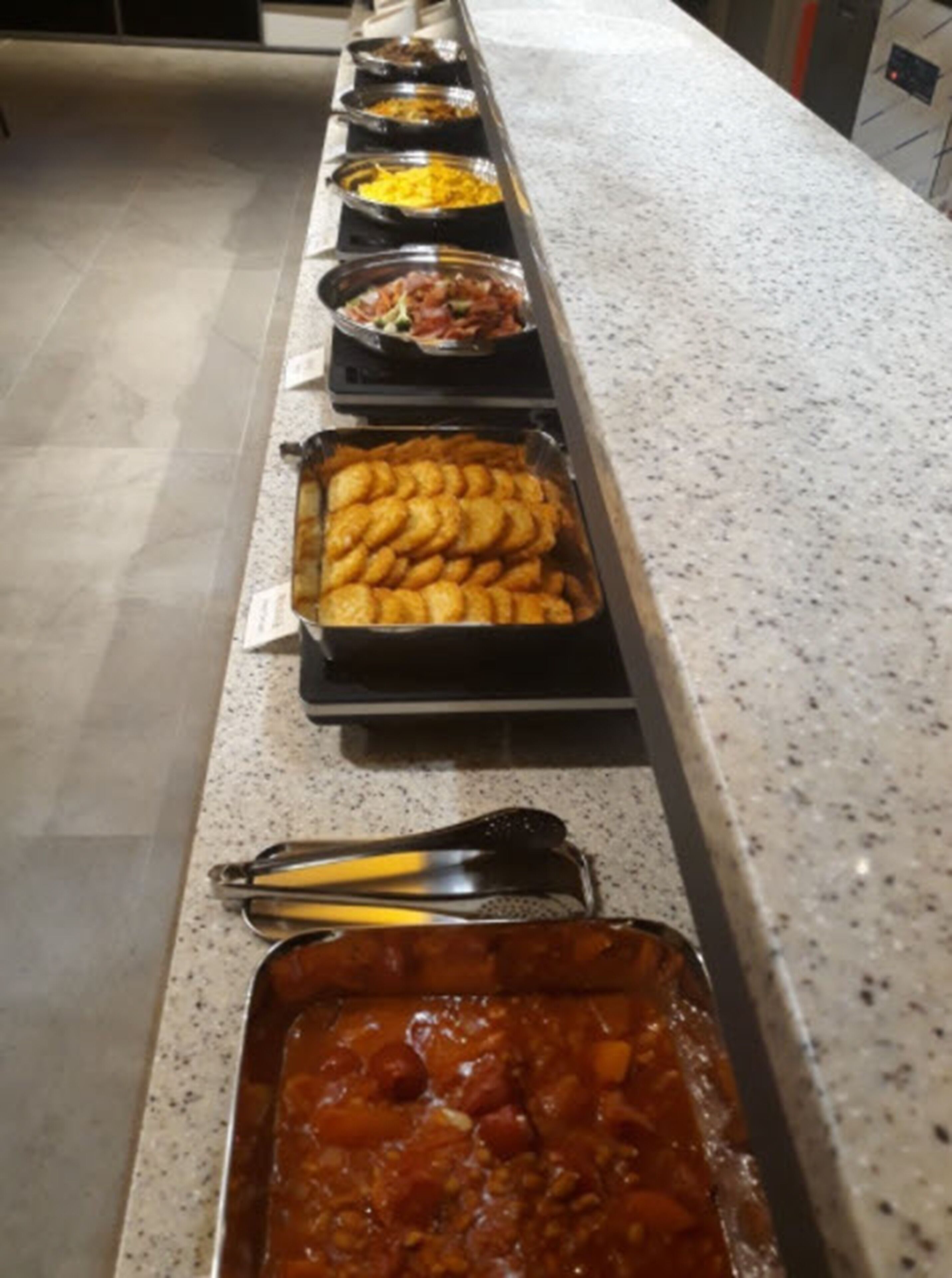 Een buffet met diverse gerechten, waaronder een schaal met goudbruin gebakken snacks, een kom gele rijst en een schotel met rode saus en stukjes.