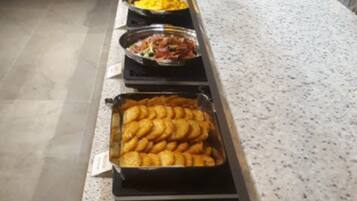 Een buffet met diverse gerechten, waaronder een schaal met goudbruin gebakken snacks, een kom gele rijst en een schotel met rode saus en stukjes.