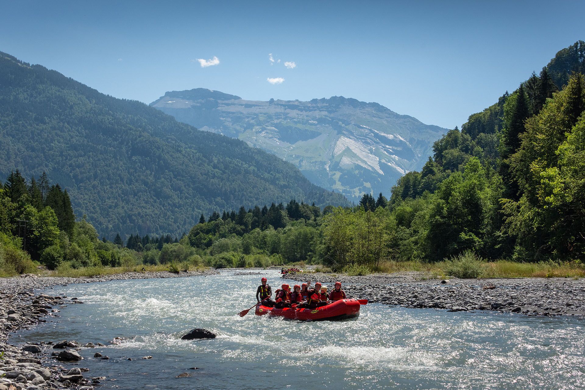 A group of people in a red raft navigating a river surrounded by forested mountains.