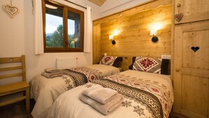 A cozy bedroom with two beds, a wooden headboard, a window with curtains, and a view of the outdoors. - Family friendly 3-bedroom apartment in Samoens close to ski bus and amenities (Samoëns)