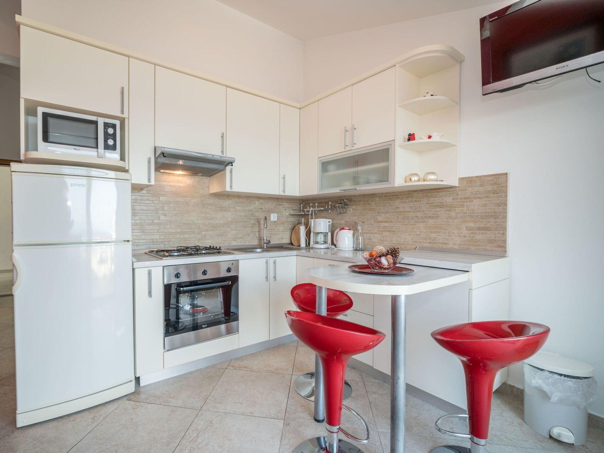 A modern kitchen with white cabinets, a microwave, a stove, and two red bar stools.