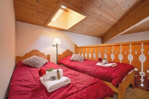 A room with two wooden beds, each with a red bedspread and white pillows. There is a skylight above the beds, and a wall-mounted lamp to the left. - Le Cristal Lognan7 Mountain View, Argentière (Chamonix), France (Argentière (Chamonix))