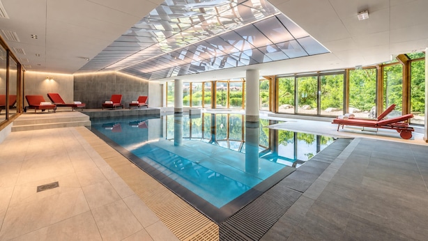 A modern indoor swimming pool with clear glass ceiling, red lounge chairs, and large windows offering a view of greenery. - Le Cristal Lognan7 Mountain View, Argentière (Chamonix), France (Argentière (Chamonix))