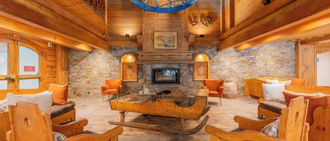 A log cabin interior with a stone fireplace, wooden furniture, and a chandelier.