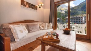 A cozy room with a wooden sofa, a table with breakfast items, and a large window offering a mountain view. - Le Cristal Lognan7 Mountain View, Argentière (Chamonix), France (Argentière (Chamonix))