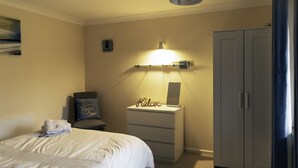 Habitación de hotel con cama, mesita de noche con lámpara, una silla, armario y un cuadro en la pared.