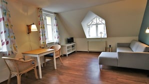Ein Zimmer mit Holzboden, einer Couch, einem Tisch, einem Sessel, einem Fernseher und einem Fenster mit Blick.