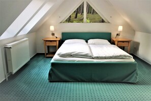 A bedroom with a sloped ceiling, a bed with white linens, two bedside tables with lamps, and a window with a view of trees. - KIWI Apartment 7 - KIWI Apartments on Lake Dreier (Alt Schwerin)
