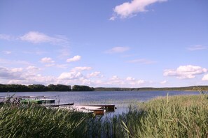 A calm lake with boats docked at a pier, surrounded by tall grass and trees. - KIWI Apartment 7 - KIWI Apartments on Lake Dreier (Alt Schwerin)
