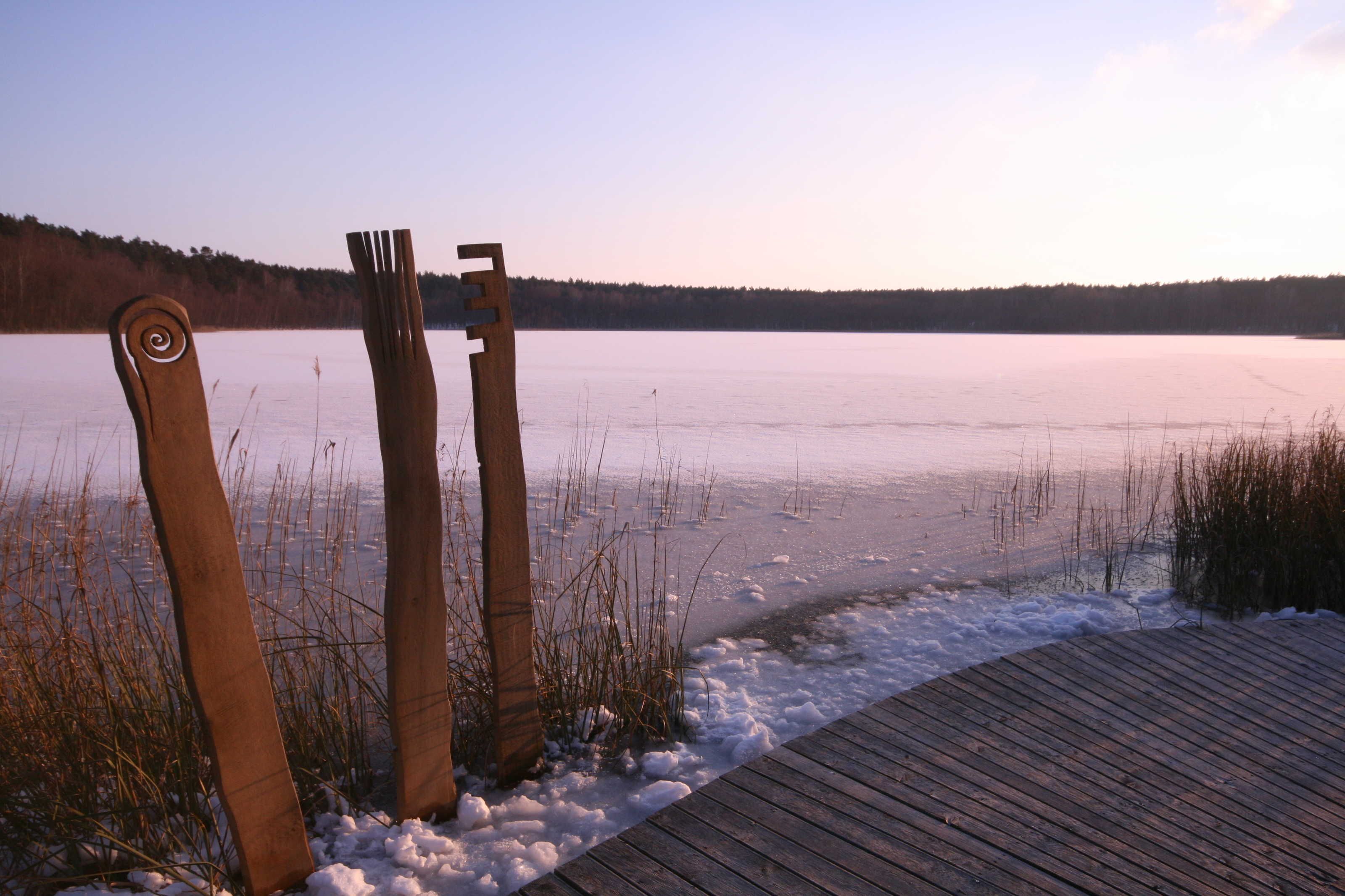 A wooden pier extending into a frozen lake with a clear sky.
