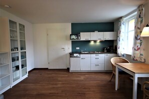 A kitchen with white cabinets, a microwave, a coffee maker, and a dining area with a table and chairs. - KIWI Apartment 7 - KIWI Apartments on Lake Dreier (Alt Schwerin)