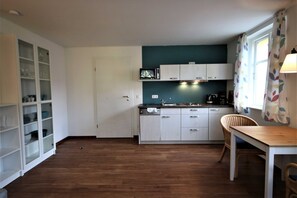 A kitchen with white cabinets, a microwave, a coffee maker, and a dining area with a table and chairs. - KIWI Apartment 7 - KIWI Apartments on Lake Dreier (Alt Schwerin)