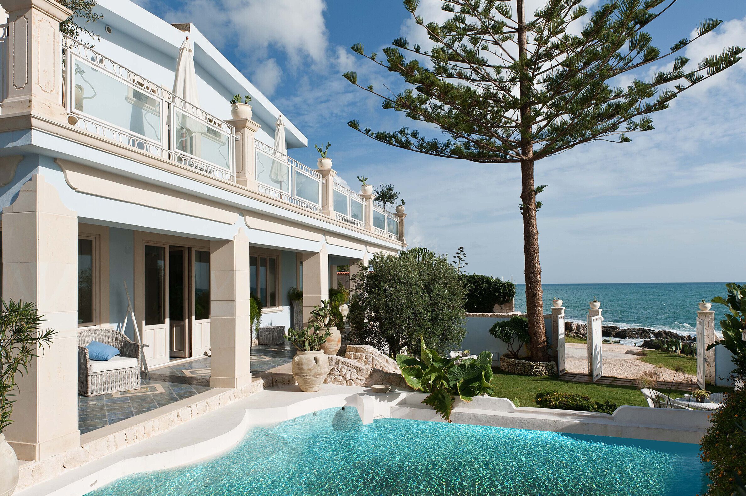 A luxurious seaside property with a swimming pool, outdoor seating, and a view of the ocean.
