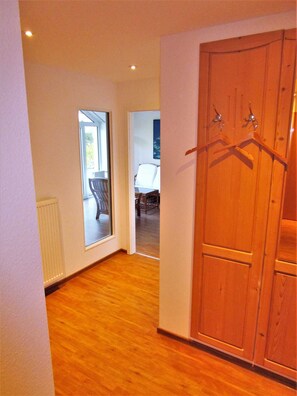 A hallway with wooden flooring, a wooden wardrobe with hangers, a chair, and a radiator.