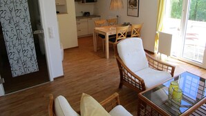 Ein Essbereich mit Tisch und Stühlen, im Hintergrund eine Küche und ein Fenster mit Vorhängen.