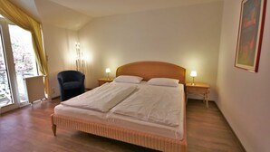 Ein Hotelzimmer mit einem großen Bett, zwei Nachttischen mit Lampen, einem Sessel und einem Fenster mit Vorhängen.
