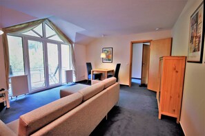 A room with a sofa, a dining table with chairs, a radiator, and a large window with curtains.