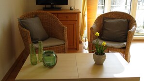 Ein Zimmer mit zwei Korbstühlen, einem Tisch, einem Fernseher auf einem Schrank und einem Fenster mit Vorhängen.