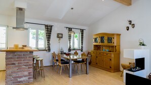 A spacious kitchen with a brick island, wooden chairs, and a wooden cabinet. - Apartment OG - Apartments Rosenhof (Tegernsee)