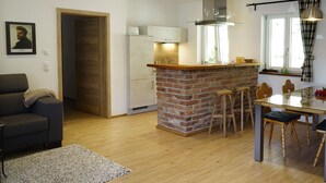 A modern kitchen with a brick island, wooden bar stools, and a dining table with chairs. - Apartment OG - Apartments Rosenhof (Tegernsee)