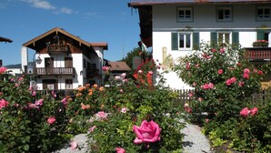 A garden with pink roses and a building with a balcony. - Apartment OG - Apartments Rosenhof (Tegernsee)