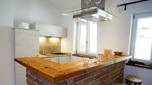 A kitchen with a wooden island, a brick accent wall, a stainless steel sink, and a window providing natural light. - Apartment OG - Apartments Rosenhof (Tegernsee)