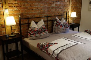 A neatly made bed with patterned pillows and a quilt, a nightstand with a lamp, and a brick wall in the background.