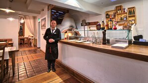 Interior de un restaurante con suelo de madera, una barra con varias botellas y una persona de pie detrás.